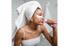 Image A woman wearing her hair wrapped in a towel brushes her teeth in the bathroom.