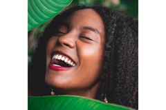 Image A smiling woman is surrounded by large tropical leaves.