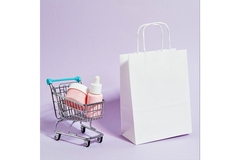 Image A miniature shopping cart filled with cosmetics is positioned next to an unbranded paper shopping bag.