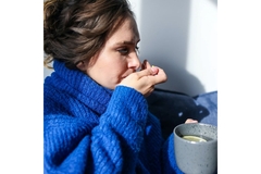 Person recovering from COVID, taking a supplement and holding a cup of tea.