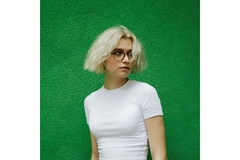 Image glasses wearing woman looks to the side in front of a green wall.