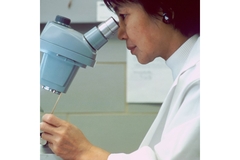 Image A woman looking into a microscope.