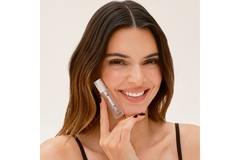 Image Model Kendal Jenner smiles while posing with a vial of Luminous Shine Teeth Serum by Moon Oral Beauty.