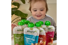A baby girl looking at packets of organic sauces and smiling.