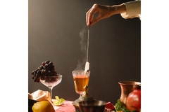 Person holding a Tea Bag submerged in a Wine Glass