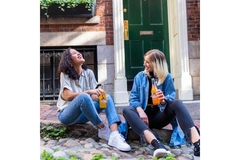 Two women sitting on the sidewalk laughing and drinking soda