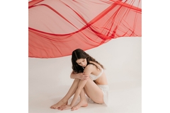 Image A woman poses artistically in a seated position underneath a billowing red fabric hanging above her.