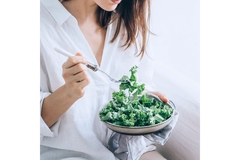 Woman eating kale on a sofa.