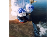 An ecologist takes water samples from a waterbody in a glass cylinder.