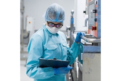 Image Person in lab coat and protective gear inspecting a factory.