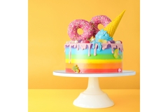 Image Colorful cake against a yellow background, kept on a white stand.