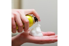 Image A person sprays hair mousse from an aerosol can onto their hand.