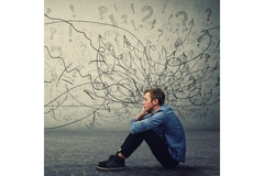 Man with mental health issues, sitting down with texts and question marks surrounding his head.
