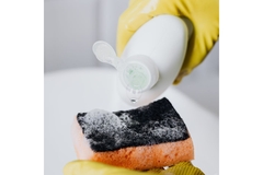 Image Person cleaning sink with sponge and wearing gloves.