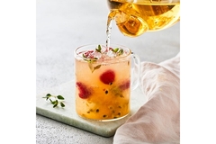 Image A glass kettle pouring light orange colored flavored water into a glass.