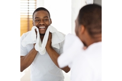 Image A man cleaning his face with a towel and looking in the mirror.