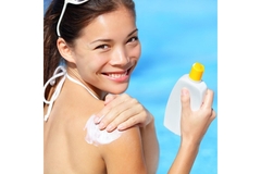 Image A smiling woman applies sunblock on her shoulder.