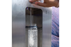 Image A hand pushing a button on a machine to fil a water bottle.