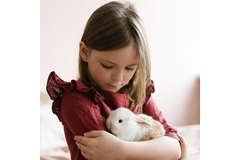 Image Young girl wearing dress holds a small rabbit against her cest