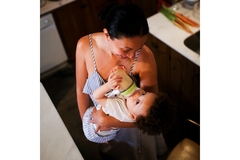 Image A mother bottle feeds her baby in the kitchen.