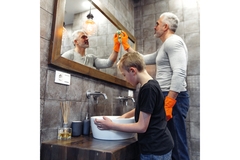 Image in a bathroom, father cleans the mirror under which the son cleans the sink.