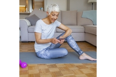 Older woman sitting on a yoga mat, looking on her phone.