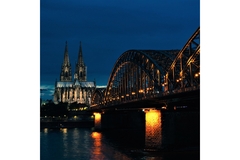 Cologne's church lit up at night with a bridge in front of it.