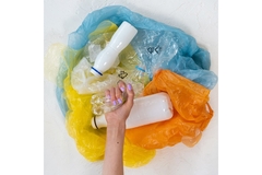 Image A hand squishing a plastic bottle on top of multi-colored plastic bags.