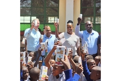 children and adults gathered outside kenyan school holding up packages of super porridge with excitement.