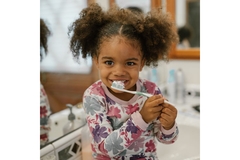 Image baby girl with curly hair sits on bathroom sink platform holding a toothbrush to her mouth