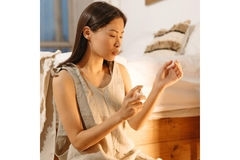 Image A woman spraying perfume on herself while sitting in a chair.