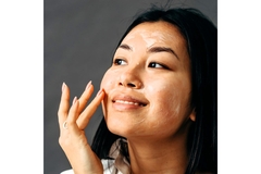 Image Asian woman looks to left with right hand touching cheek with sunscreen on face