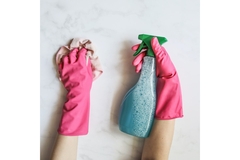 Hands in pink cleaning gloves holding a blue spray bottle.
