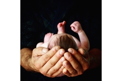 Image A man holds a baby in his hands.