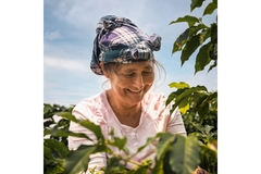Smiling old farmer woman looks down to right, among trees.