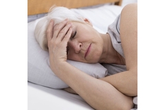 Senior woman having difficulty sleeping, lying in bed with hand to her head.