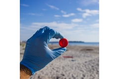 Image A hand with a glove on holding a cap in front of a beach view.