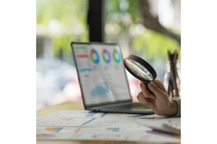 Image Computer open with graphs, person looking at reports with a magnifying glass.