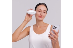 A woman holding a skin care device to her cheek while holding her phone in the other hand.