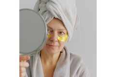 Image An older woman with under eye patches while looking in a small mirror.