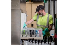 Image man putting a crate full of bottles through a washing conveyor belt
