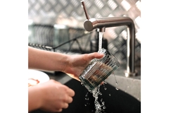 Image Two hands washing a cup under water in a sink.