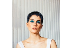 Image Woman with short pixie hair, wearing heavy eye makeup poses looking straight.