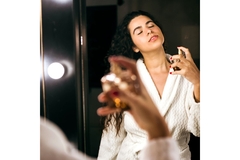 Image A woman spraying perfume on her neck from the angle of looking in a mirror.
