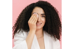 Image woman with curly hair in a bathrobe covers one eye with a cotton pad