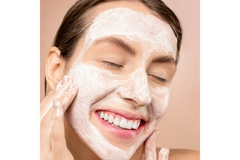 Image A woman smiling while washing her face in front of a pink background.