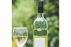 Image The top of a wine bottle and wine glass in front of leaves.