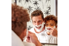 Reflection of father and son wearing shaving cream on face in mirror.