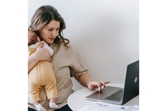 Image Woman holding a baby, looking at her computer.