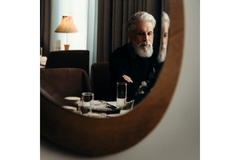 Image reflection of bearded old man in mirror sitting by a dressing table